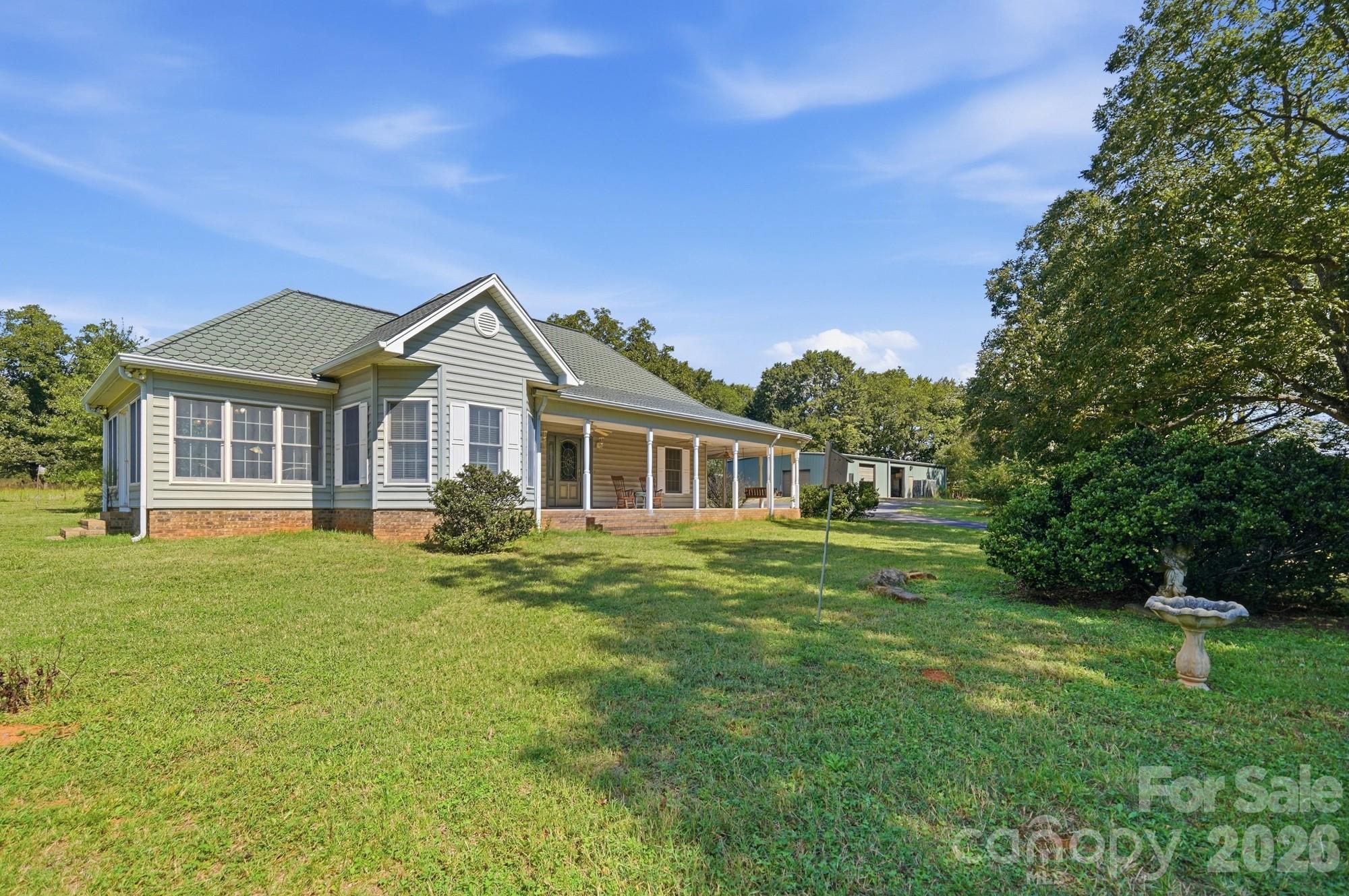 Gray-sided home with a covered front porch, broad lawn, mature trees, and a small outbuilding.