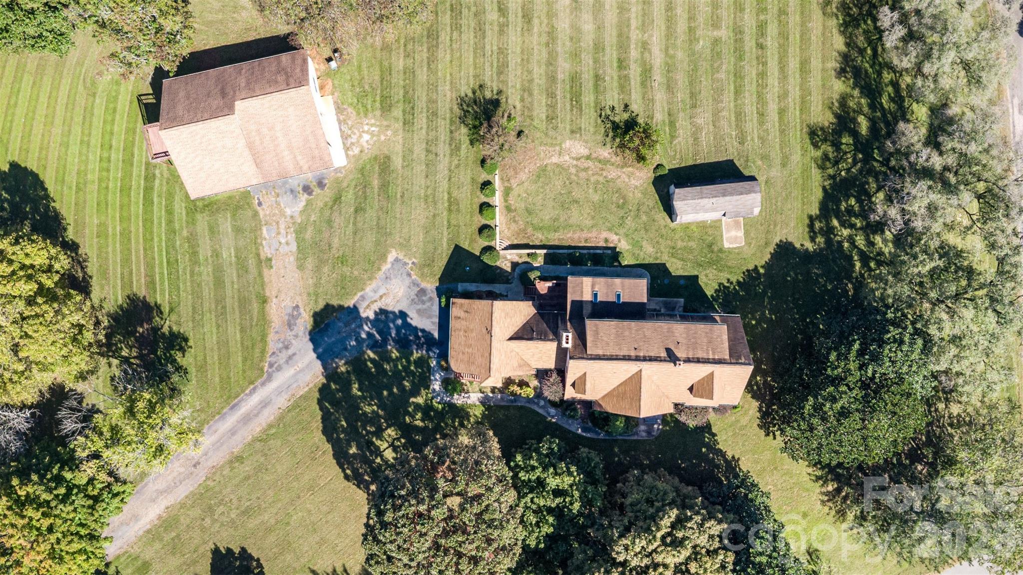 Aerial view of two houses and a detached outbuilding on a large lawn surrounded by mature trees.