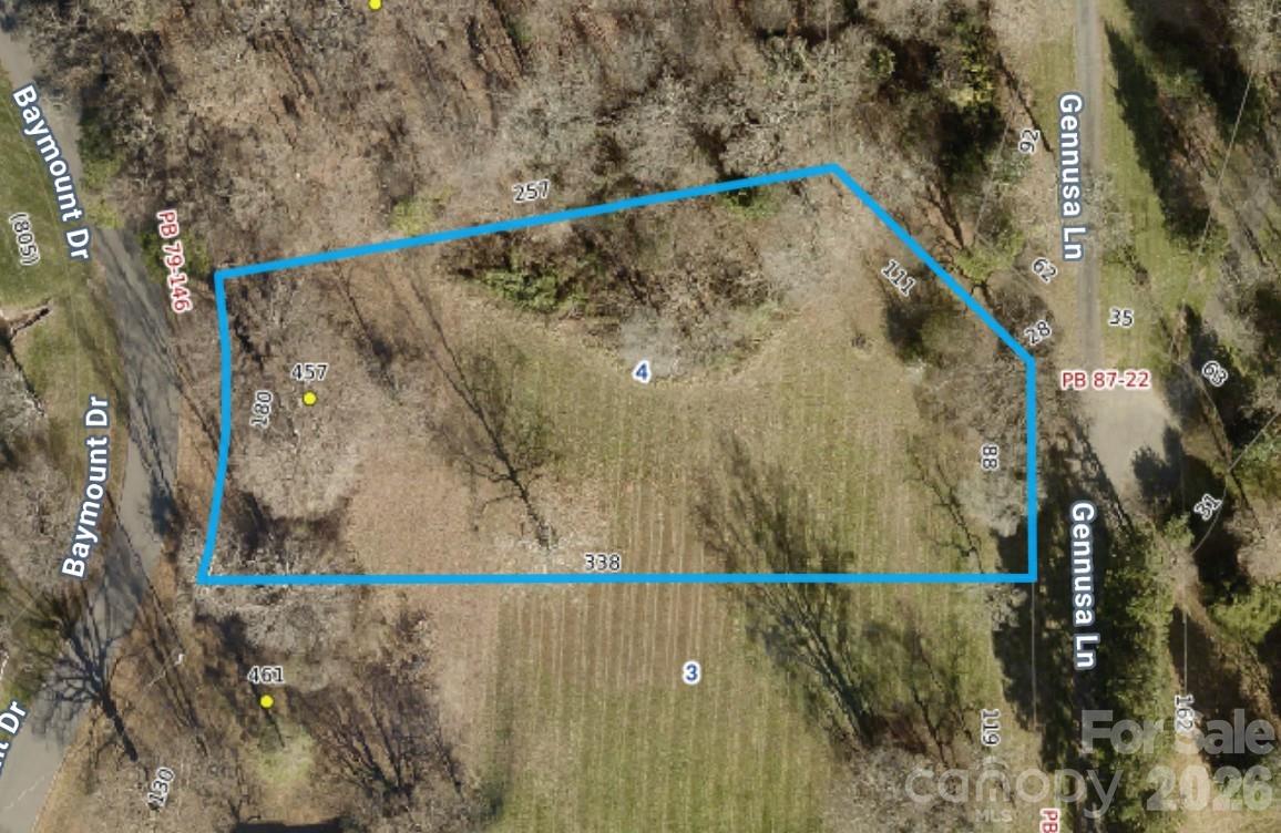 Aerial view of the wooded 457 Baymount Drive lot outlined in blue between two roads.