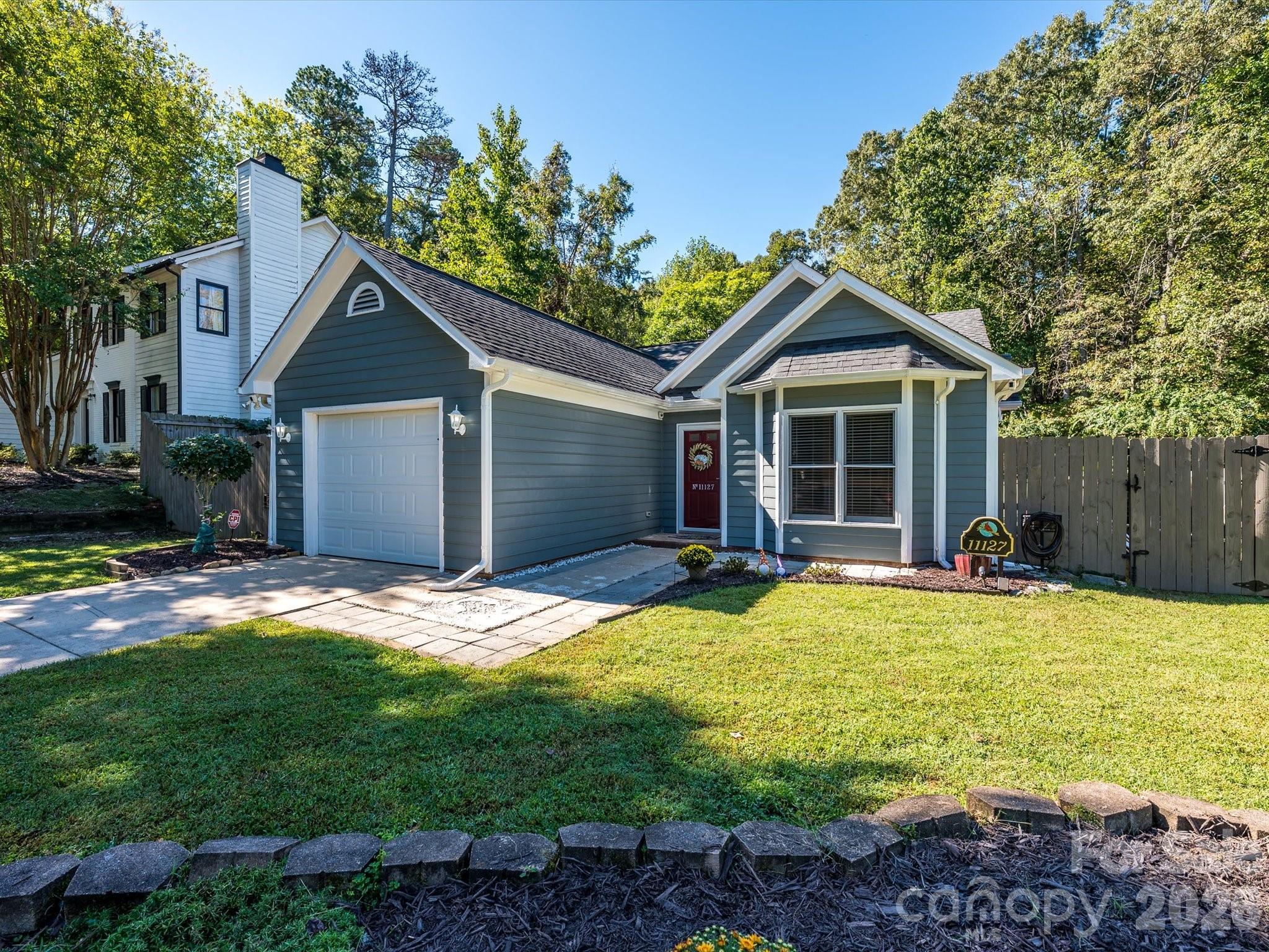 Blue-gray house with an attached garage, red front door, and fenced yard.