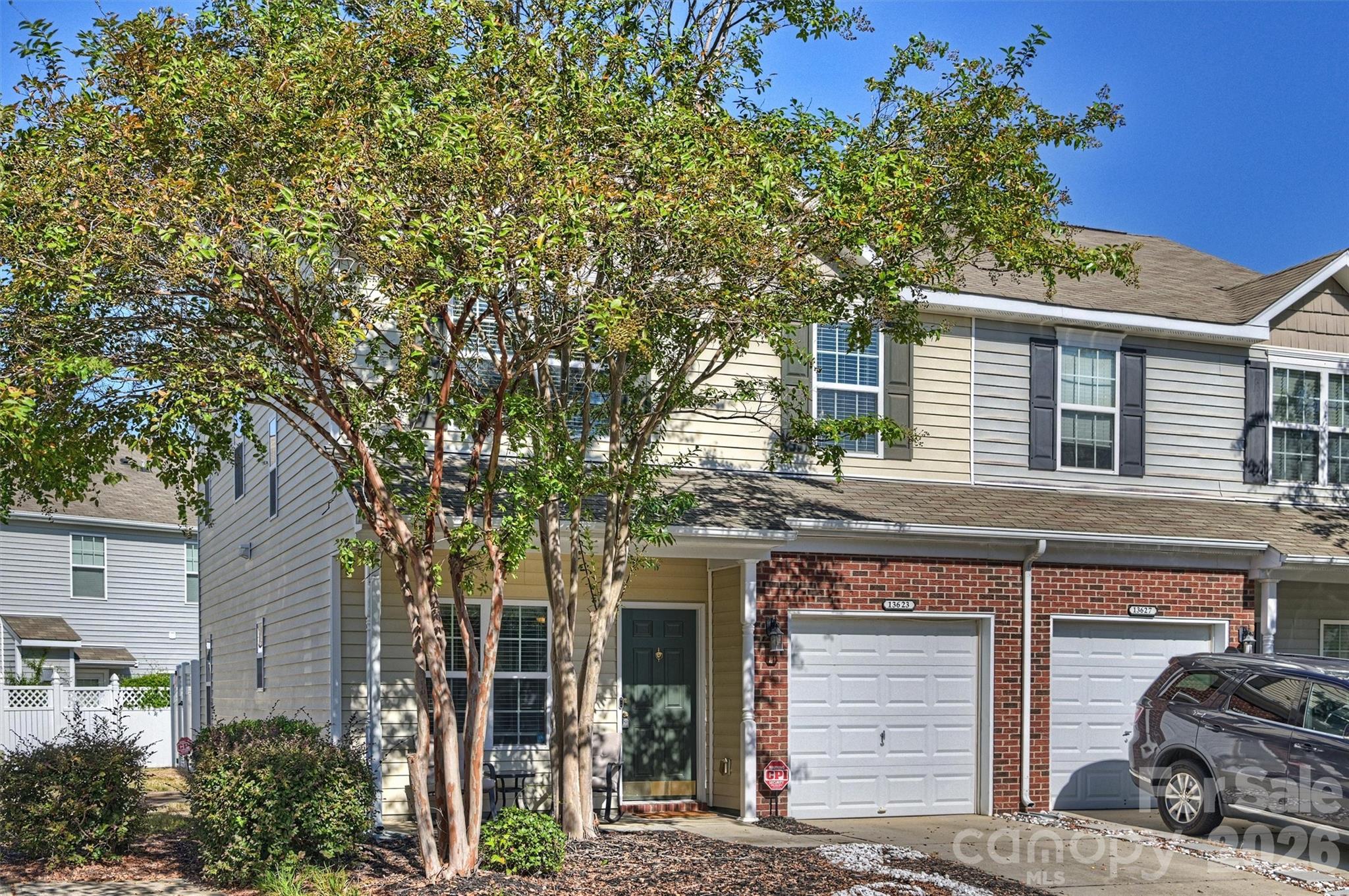 Two-story attached home with a brick garage facade and mature trees across the front.