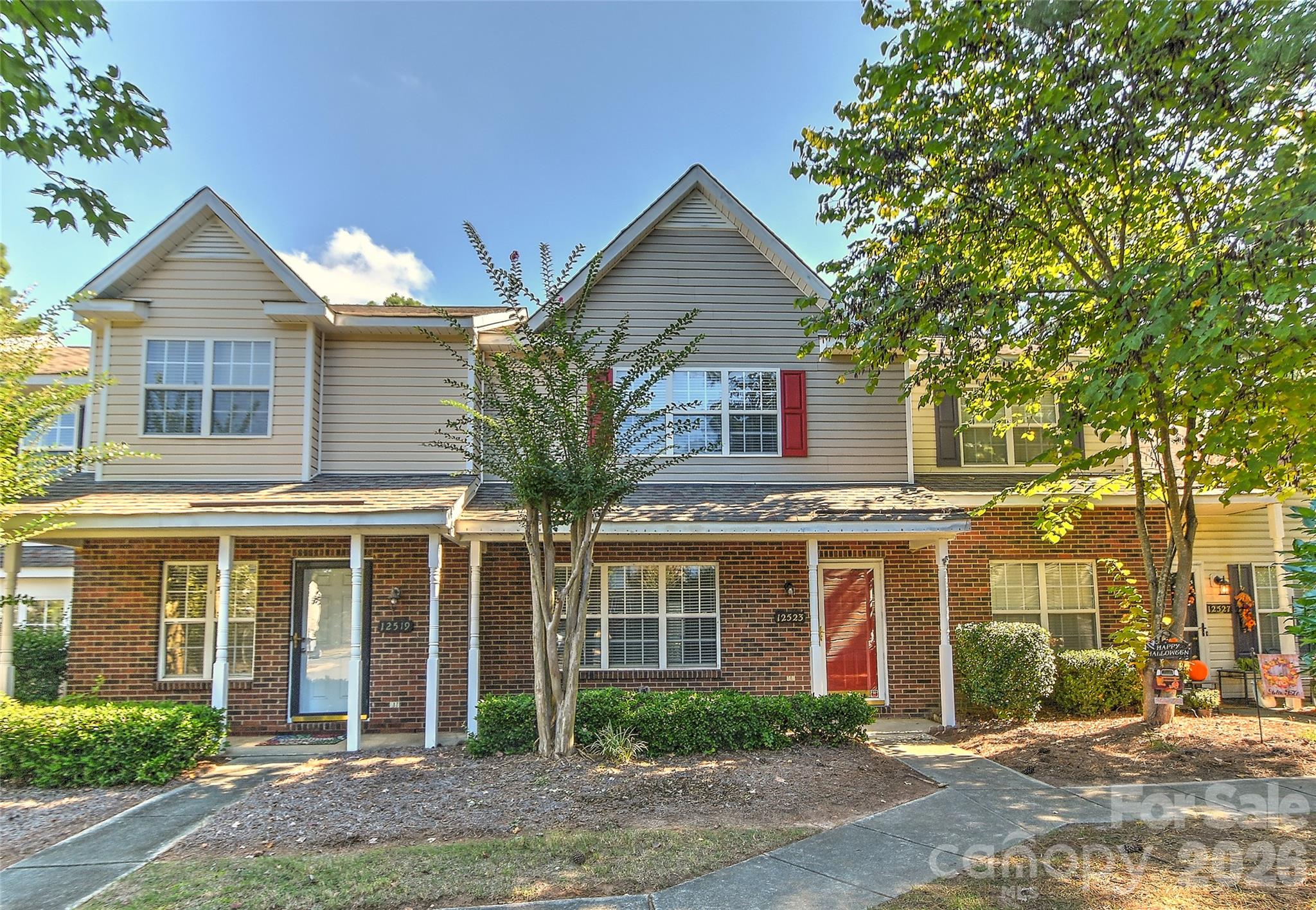 Townhouse at 12523 Bluestem Lane with a red front door, brick lower level, and leafy front yard.