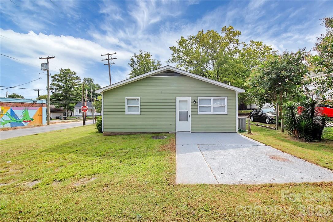 Green single-story house with white trim, a front lawn, and a concrete driveway.