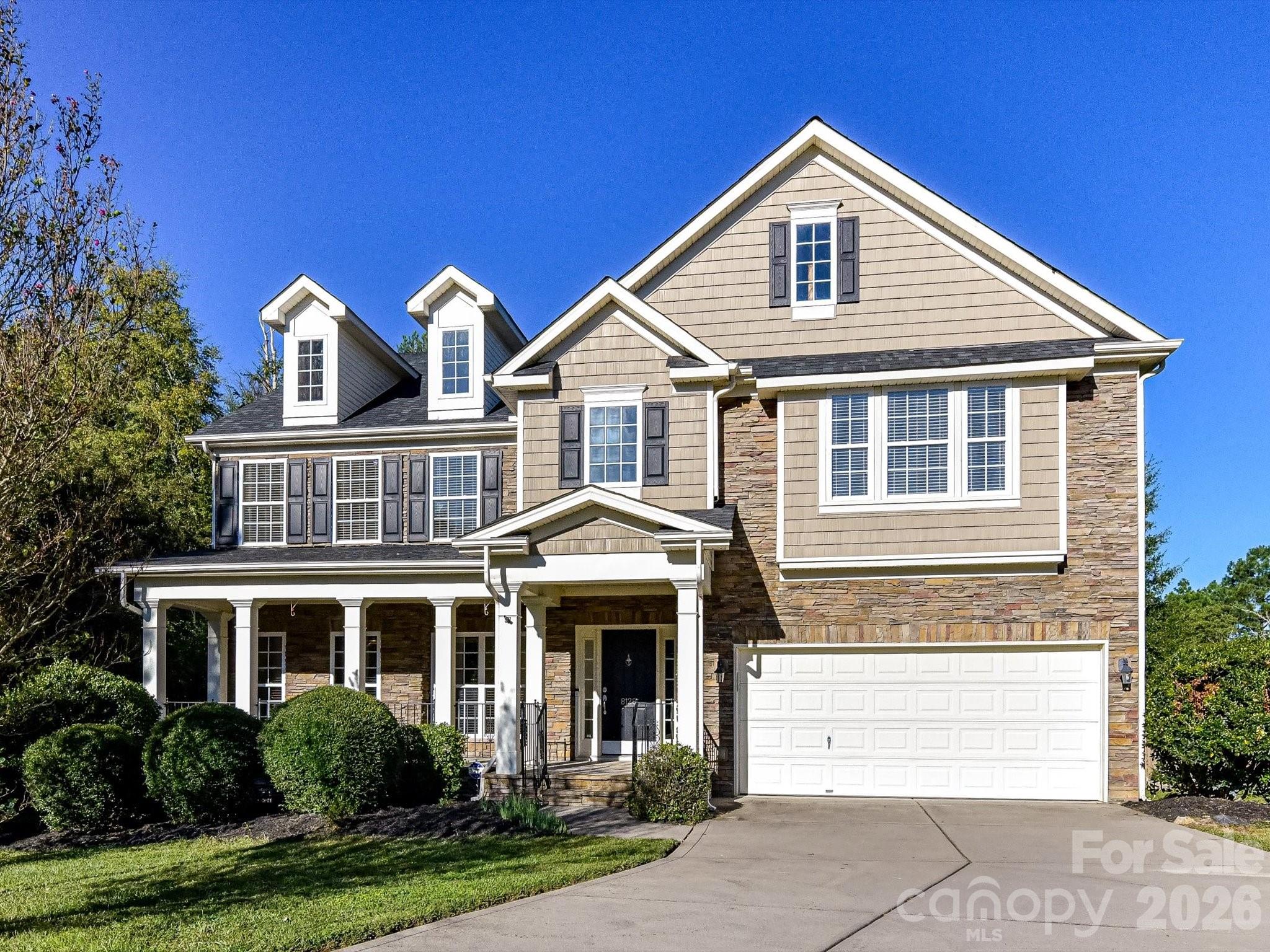 Two-story tan house with stone accents, a covered porch, and an attached double garage.