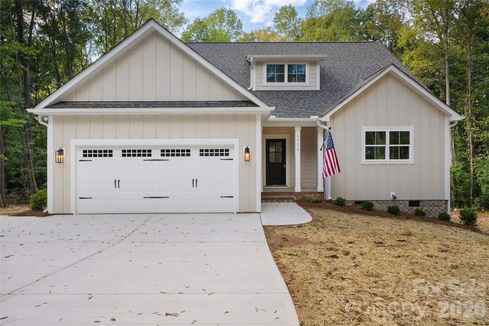 Cream house with a two-car garage, American flag, and wide concrete driveway.