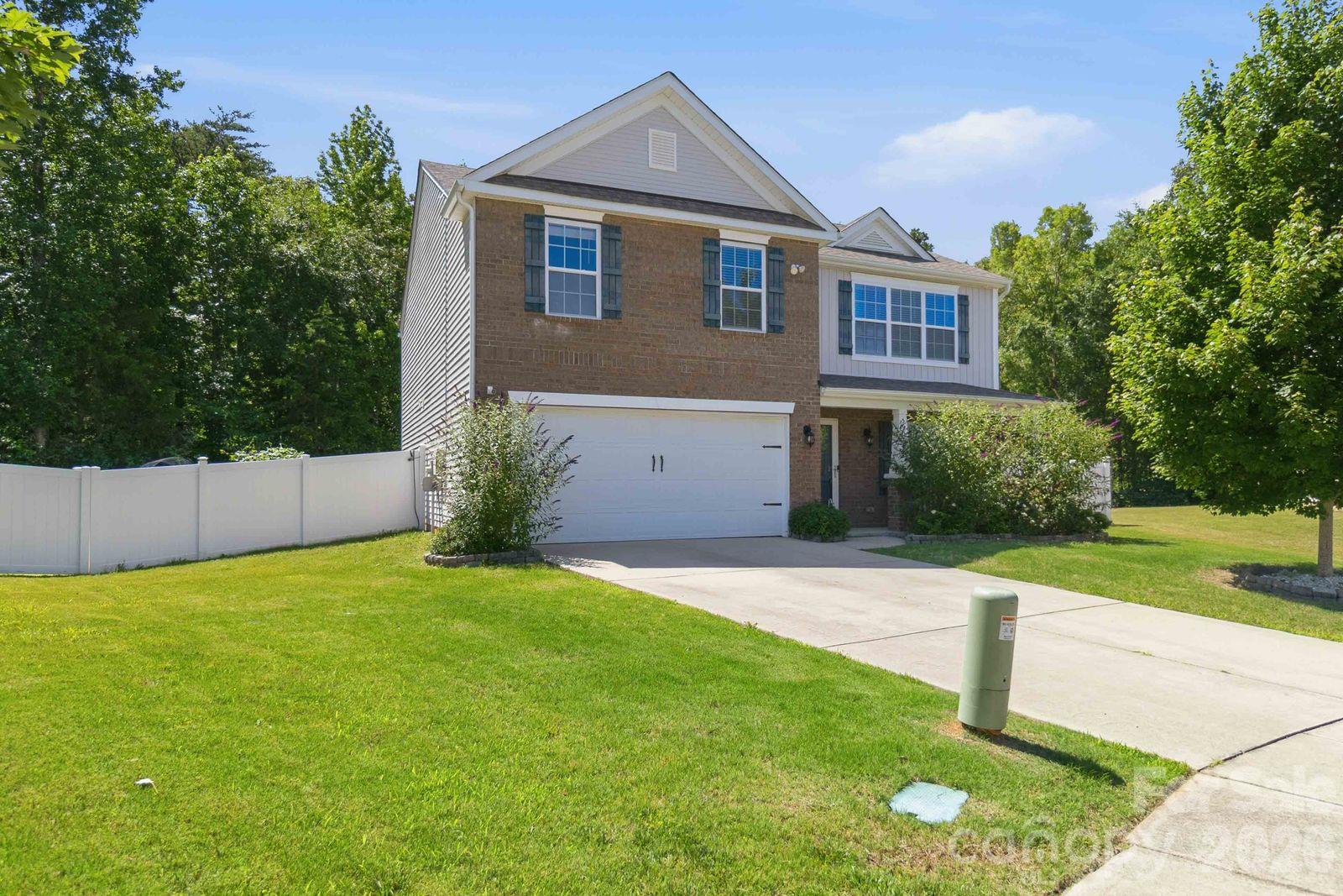 Two-story brick-and-siding home with a two-car garage, white privacy fence, and landscaped front lawn.