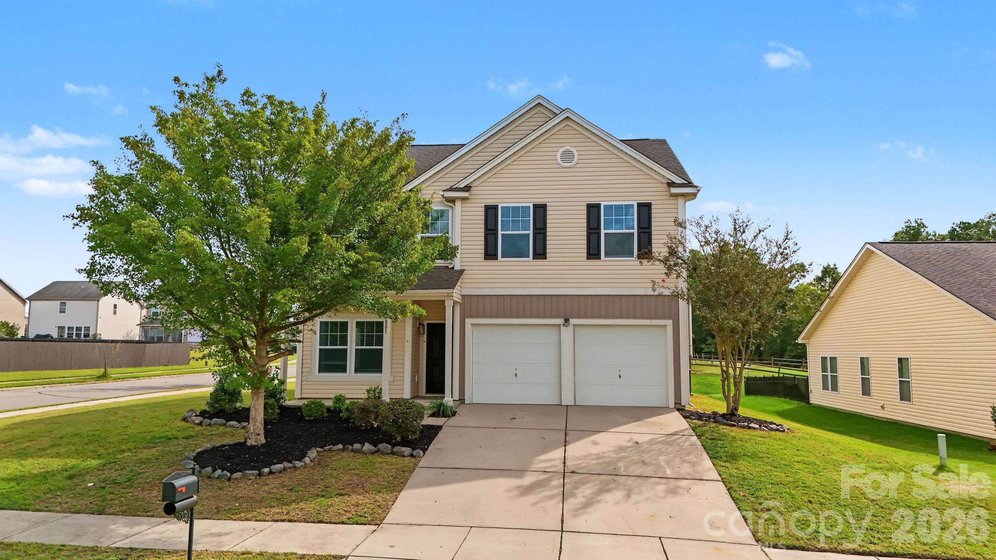 Two-story beige house with a double garage, wide driveway, and mature front-yard trees.