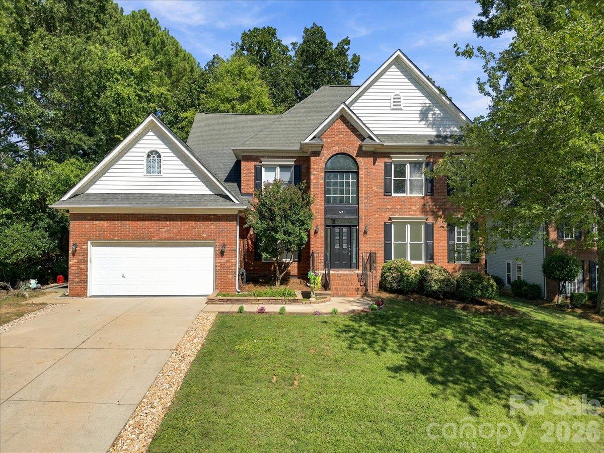 Two-story brick house with white gables, an arched window, attached garage, and broad front lawn.