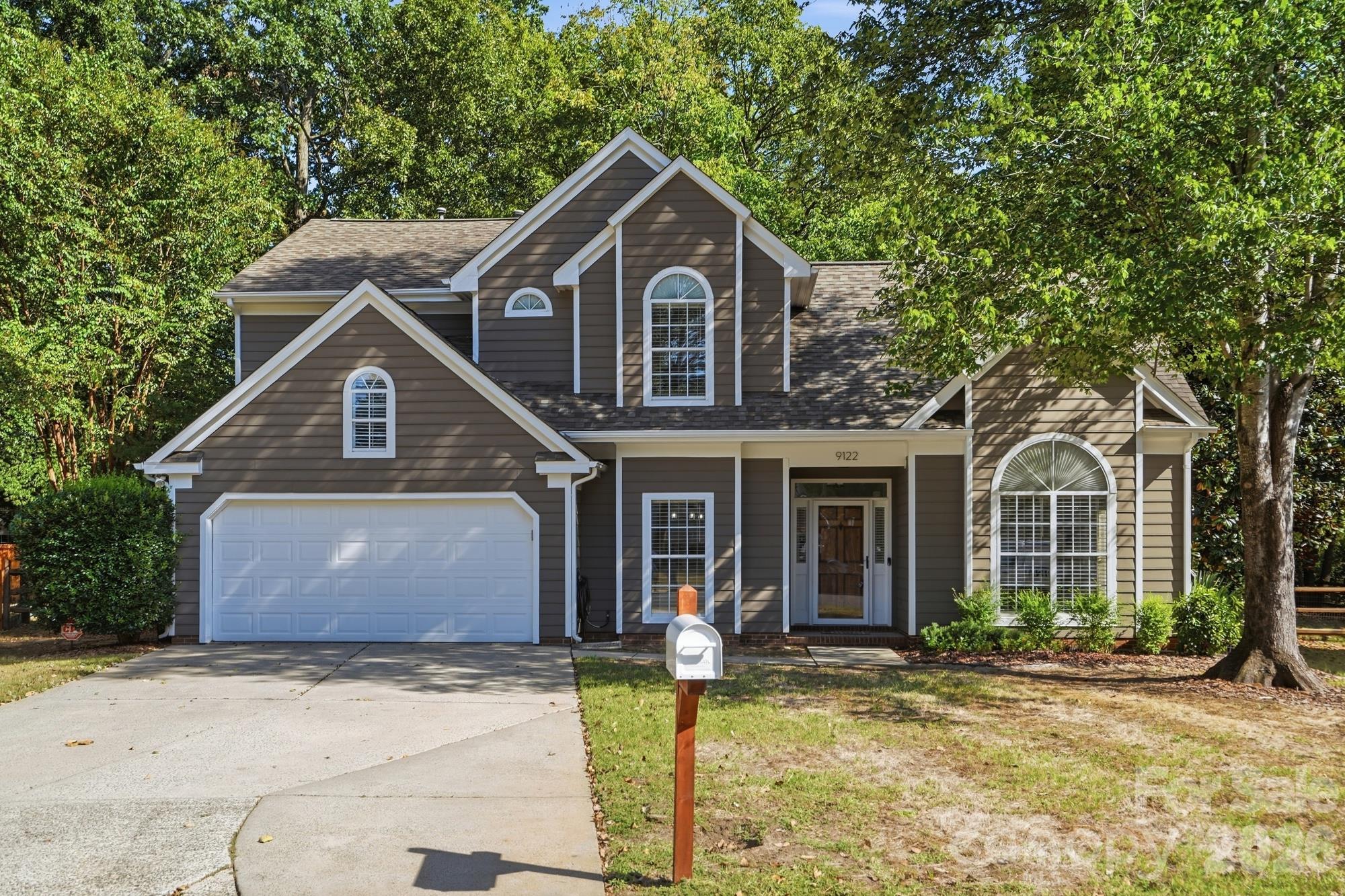 Two-story brown-sided home with white trim, arched windows, double garage, and a front mailbox.