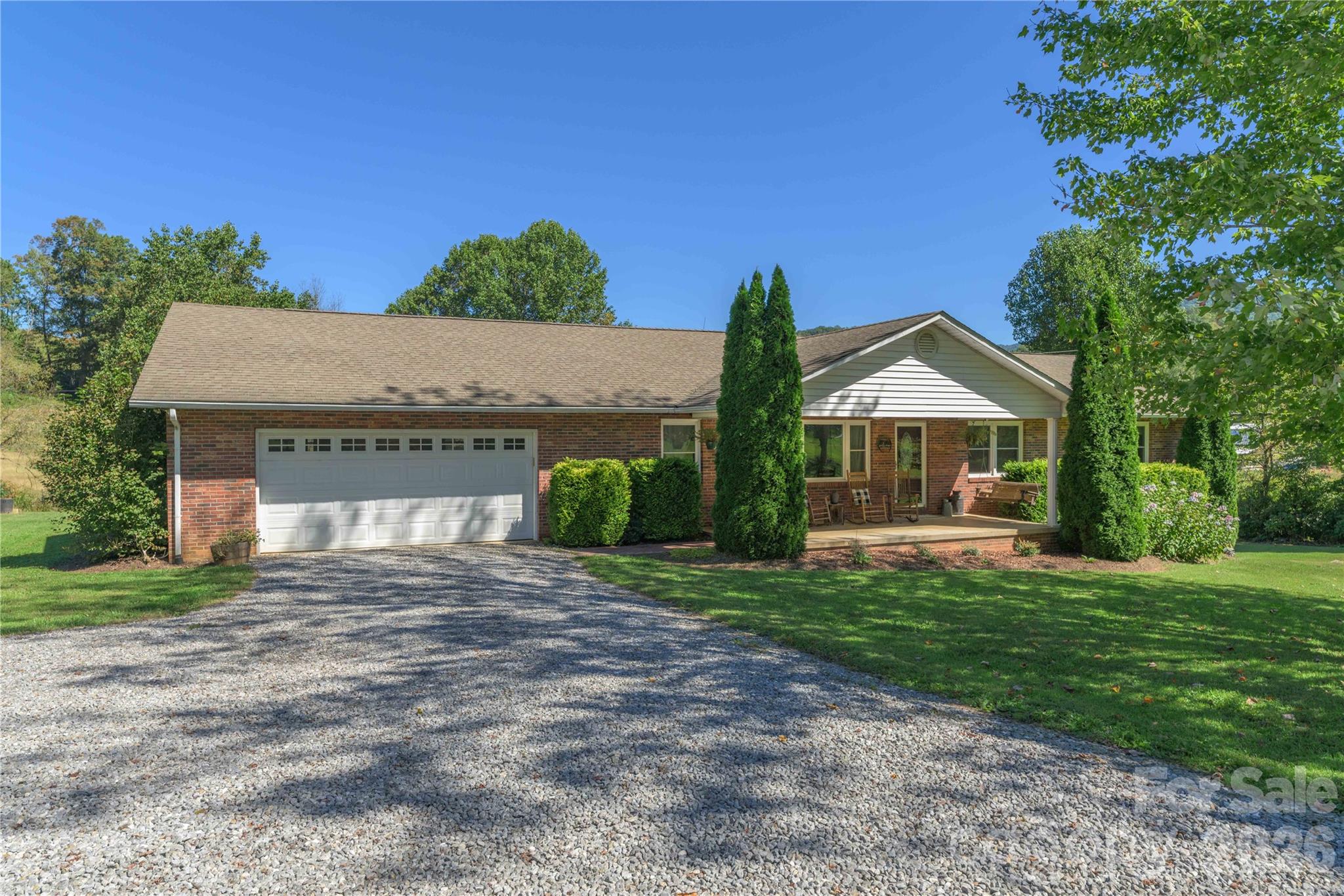 Single-story brick ranch home with a two-car garage, covered porch, and gravel driveway.