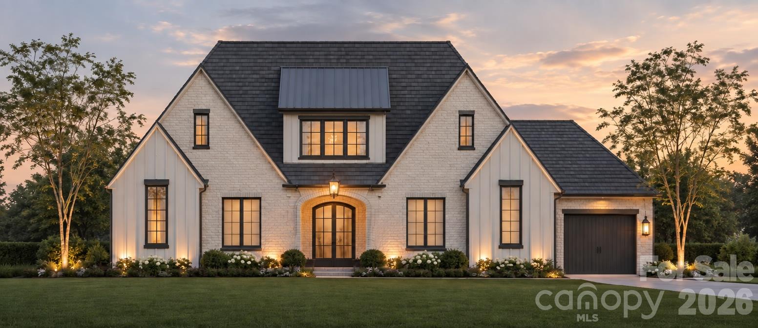 White brick house with a dark roof, attached garage, and illuminated landscaping at dusk.