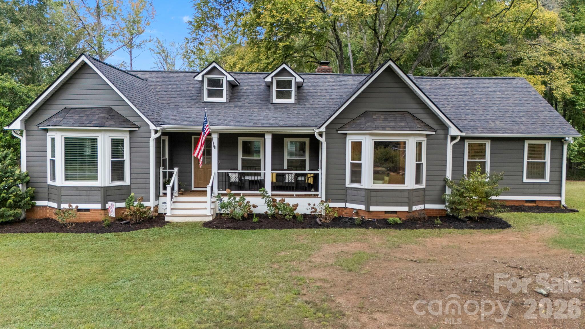 Gray home with white-trimmed bay windows, roof dormers, and a covered front porch.