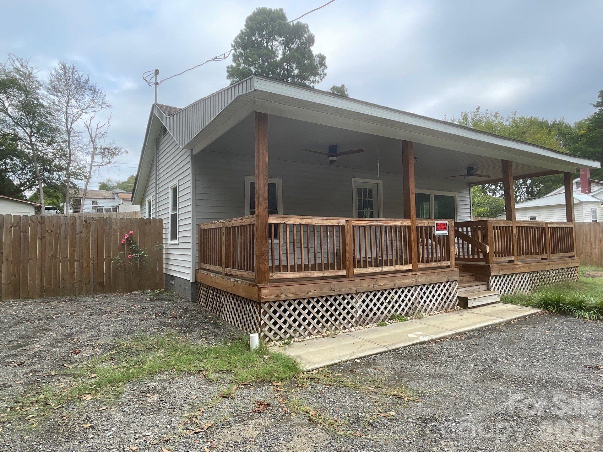 Gray house with a wide covered wooden porch and gravel driveway.
