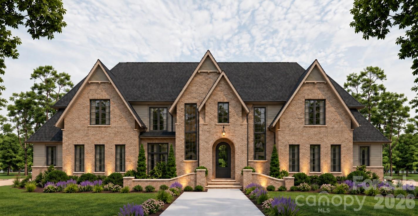 Large brick house with steep gables, an arched entry, and purple flowers lining the front walkway.
