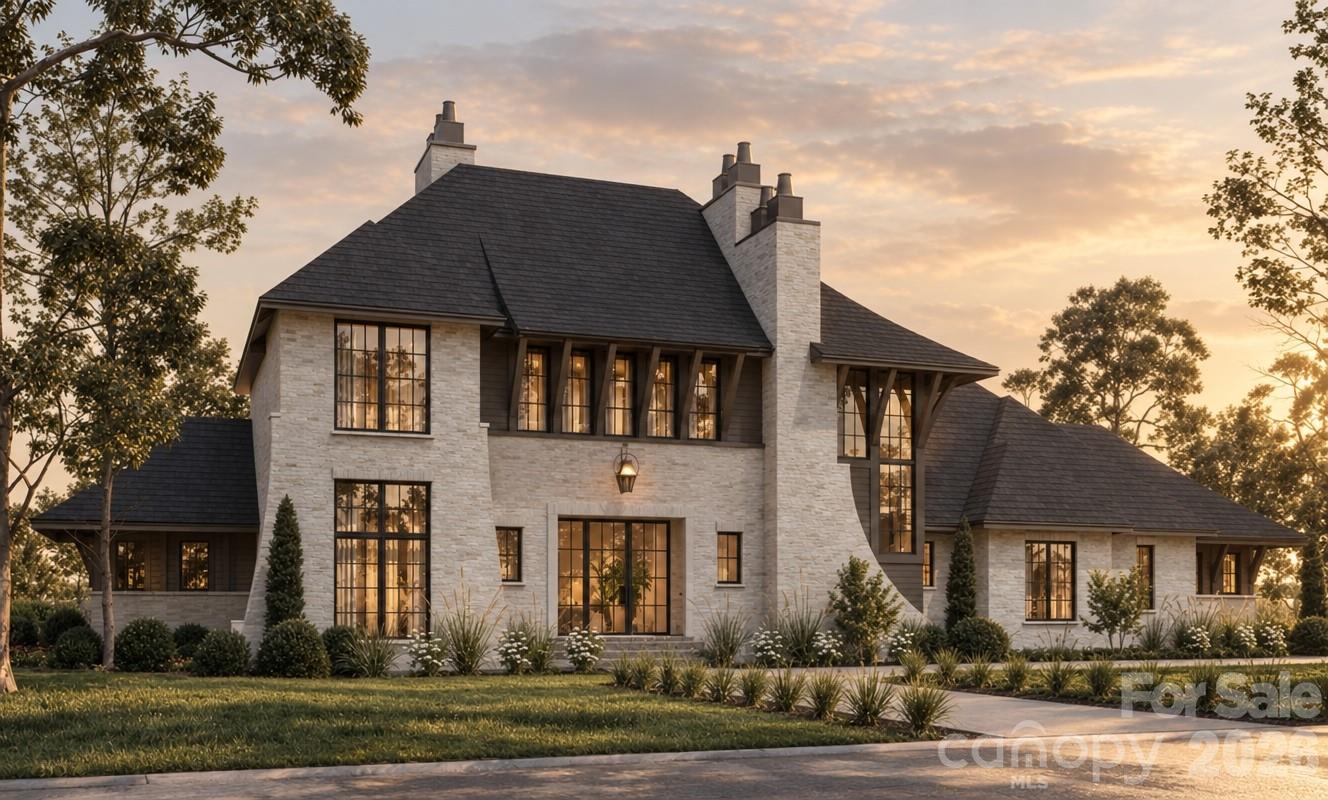 Two-story stone house with a dark roof, tall windows, and landscaped grounds at sunset.