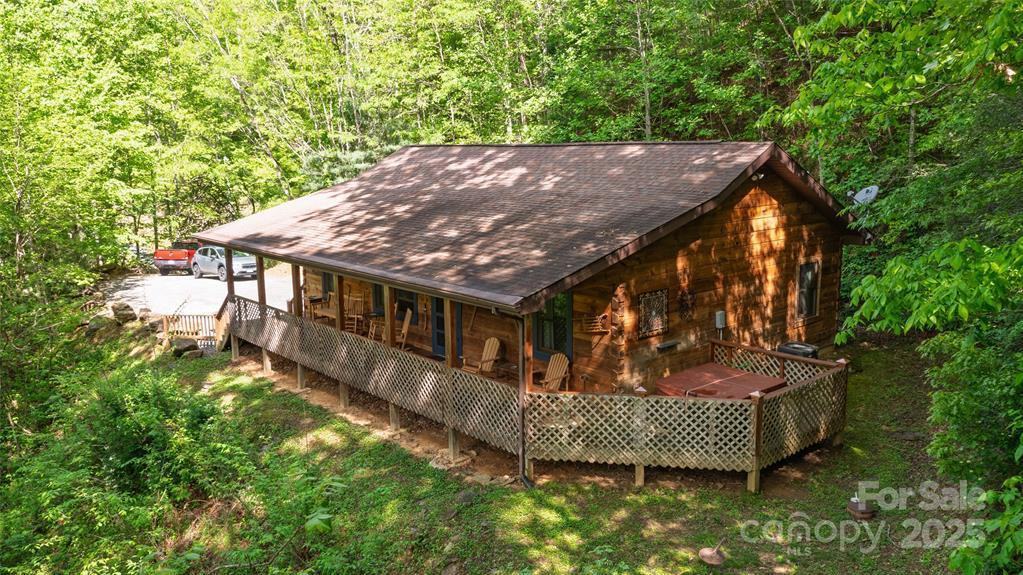 Wooden cabin among trees with a long covered porch and lattice-sided deck.