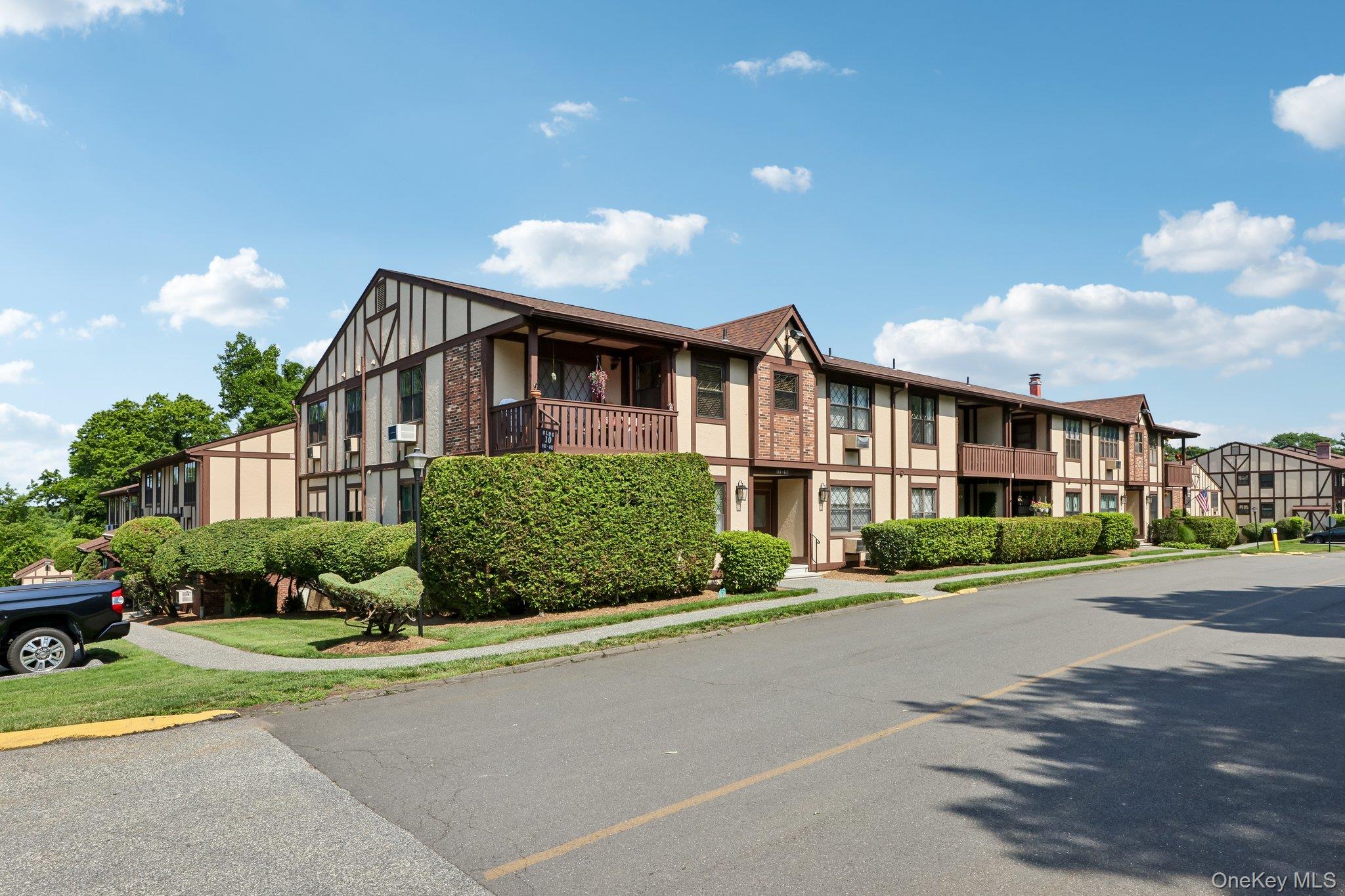 Two-story Tudor-style residential building with balconies and trimmed hedges along the street.