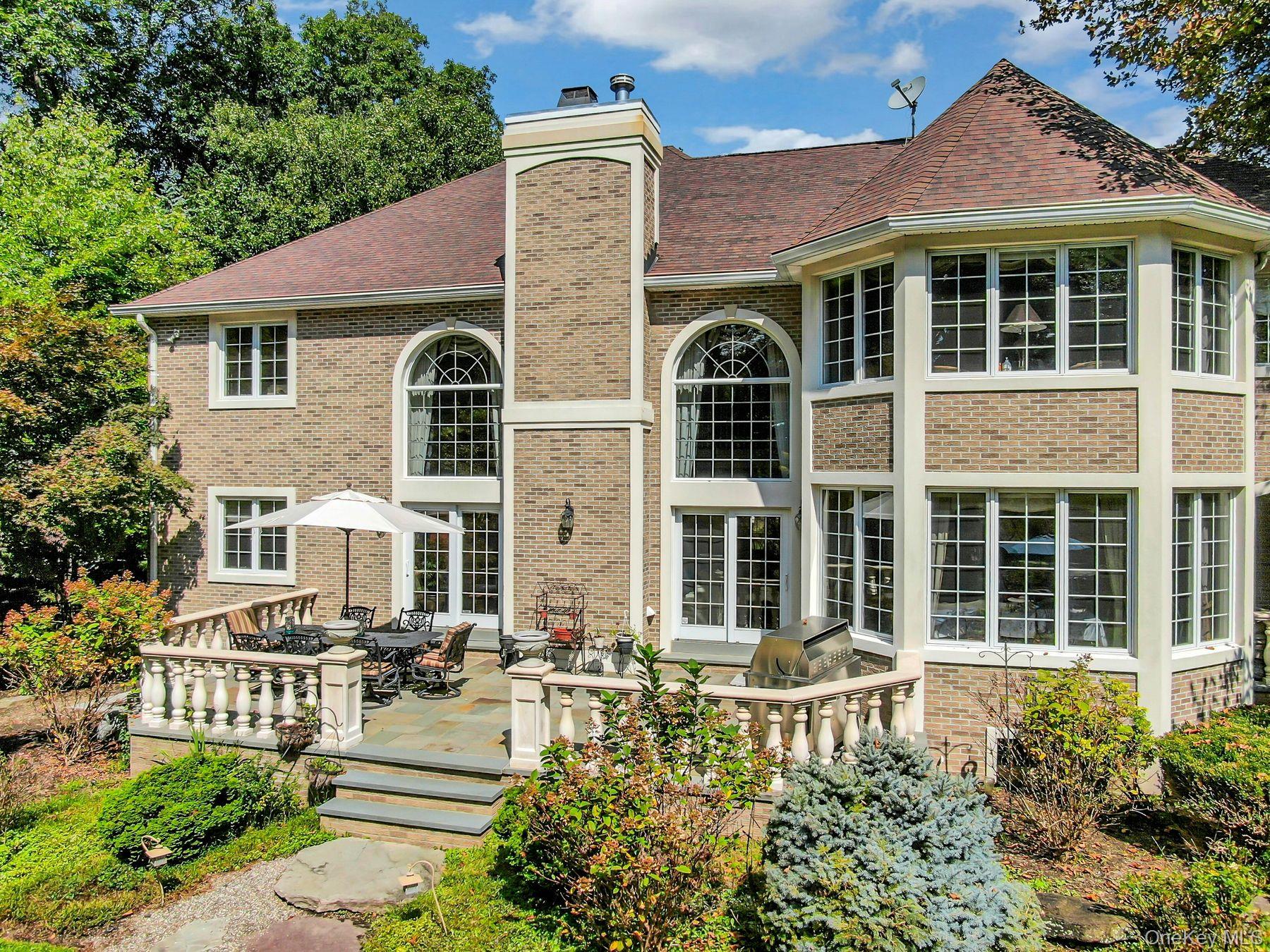 Brick home’s rear exterior with a stone patio, outdoor dining furniture, and grill.