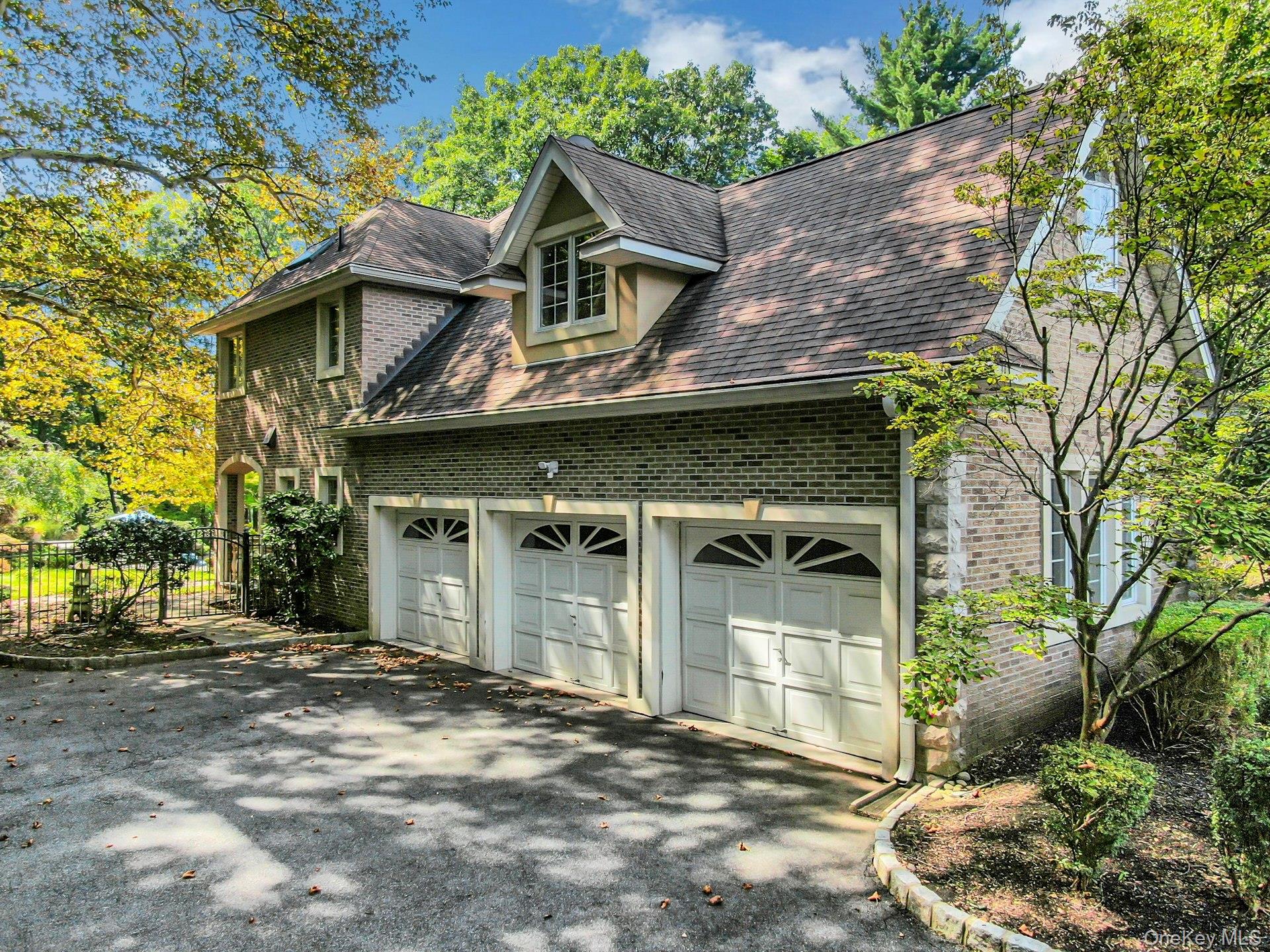Brick house with three white garage doors and a steep roof, framed by leafy trees.