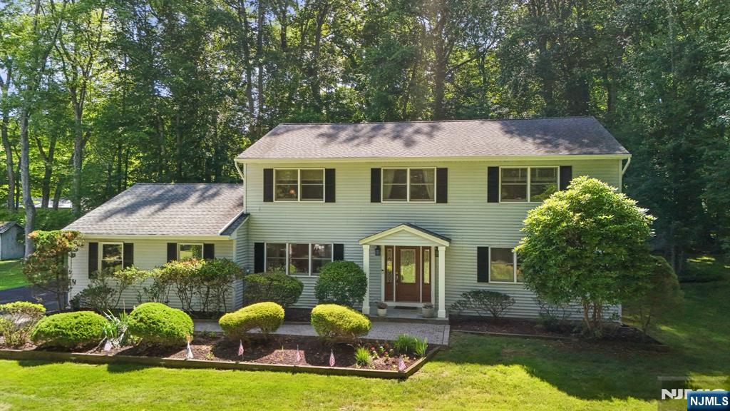 Two-story home with black shutters, a covered entry, landscaped garden beds, and a broad lawn.