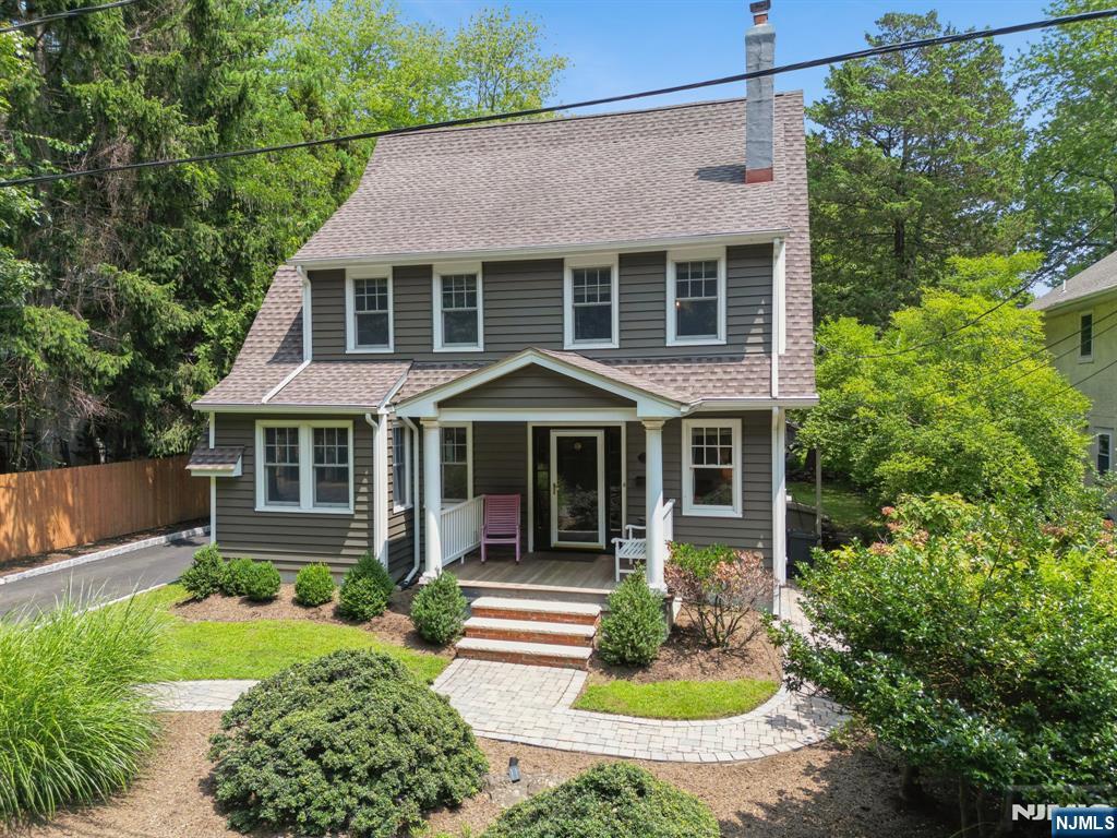 Two-story gray house with a covered porch, curved paver walkway, and landscaped yard.