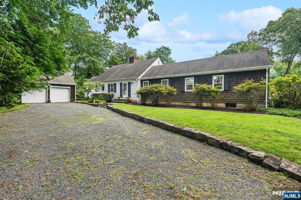 Single-story shingle-sided home with detached garage beside a broad gravel driveway.