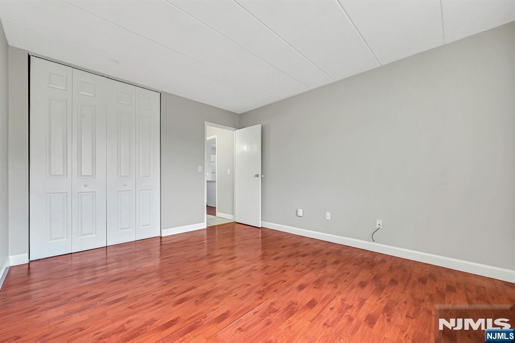 Empty bedroom with reddish wood flooring, gray walls, and white closet doors.