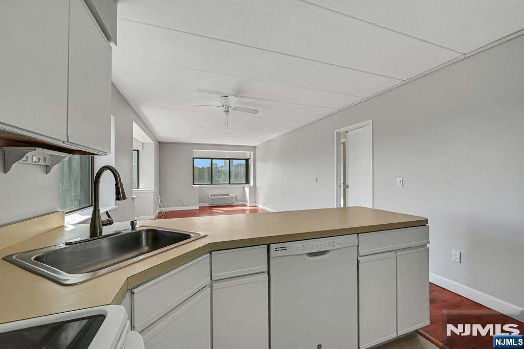 Vacant kitchen with a long counter and sink opening into a sunlit living area.