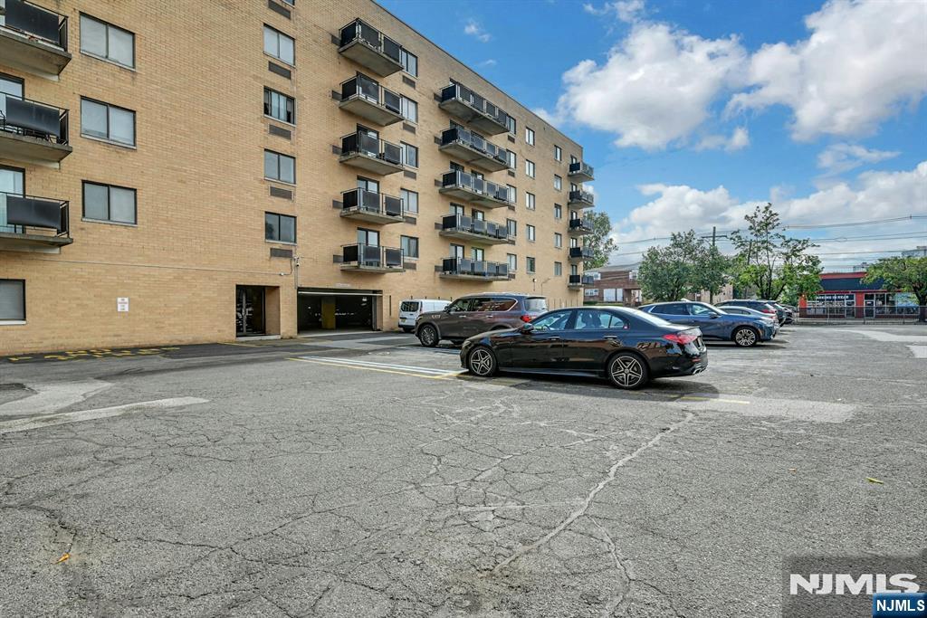 Tan brick apartment building with balconies overlooking a parking lot with parked cars.