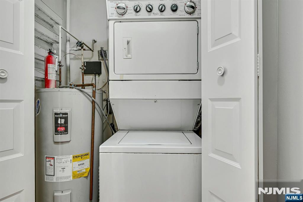 Laundry closet with a stacked washer-dryer beside a water heater and exposed pipes.