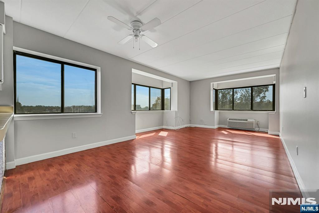 Vacant living room with reddish hardwood floors, three large windows, and a ceiling fan.