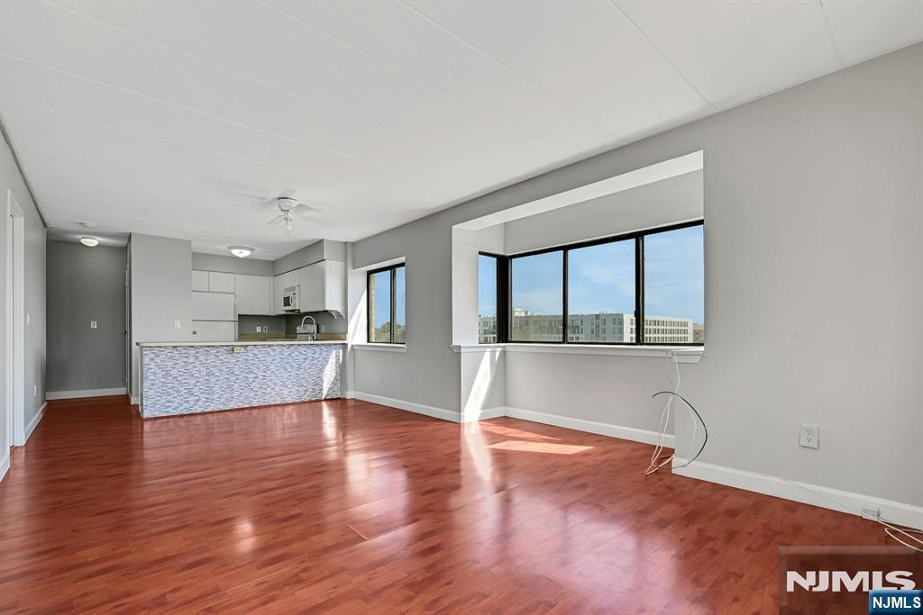 Open living area with reddish wood floors, large windows, and a white kitchen peninsula.