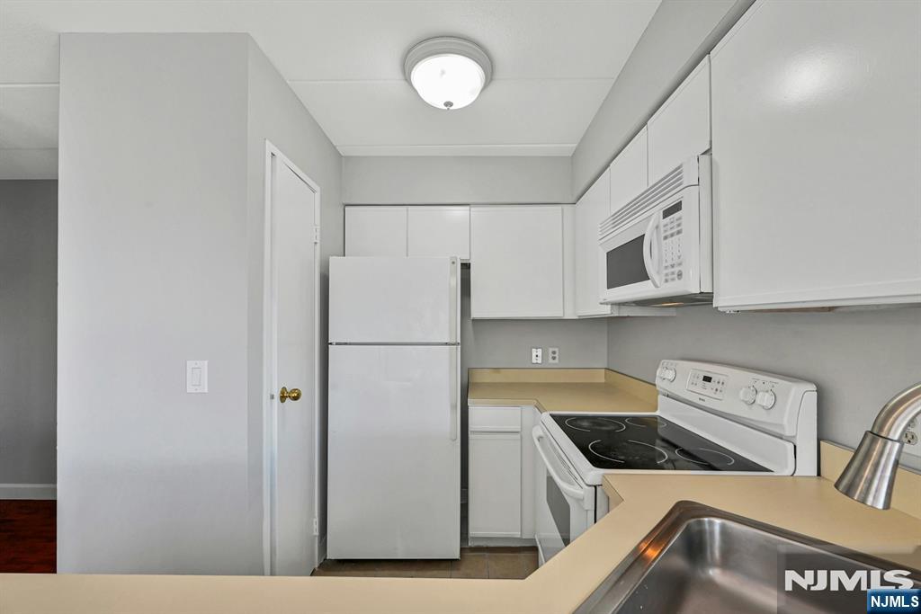 Compact kitchen with white appliances, tan counters, and a stainless steel sink.