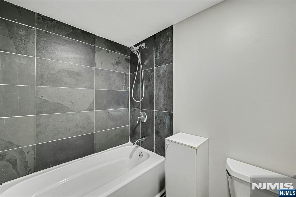 Bathroom with a white tub and shower against dark gray tiled walls.