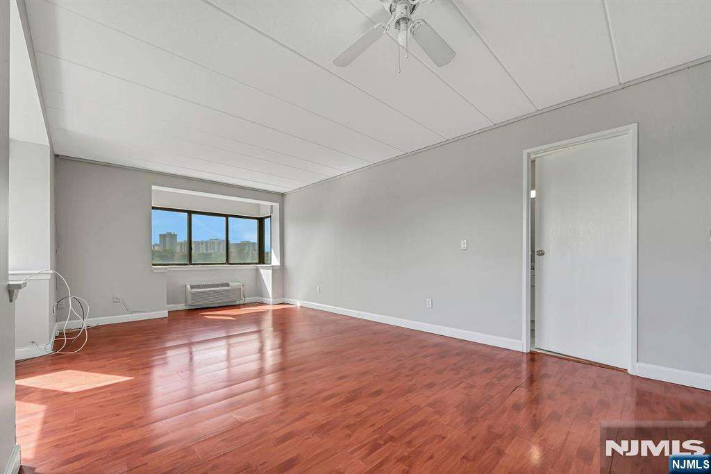 Vacant room with reddish hardwood floors, a wide window, and a ceiling fan.