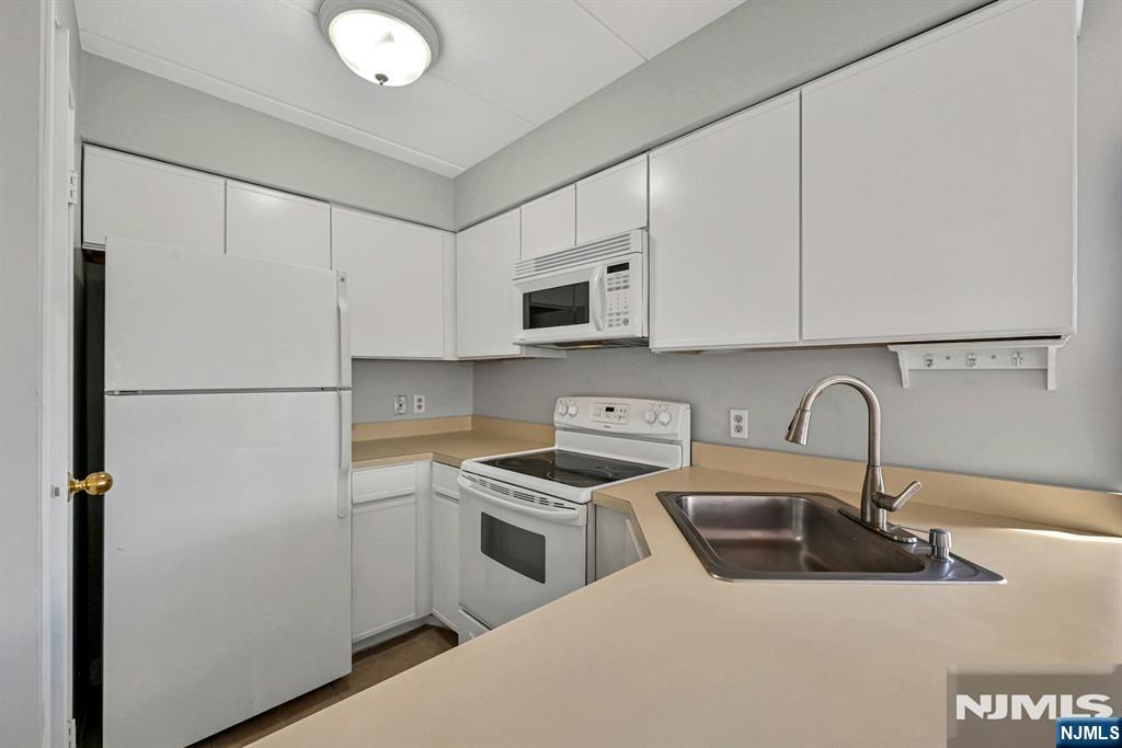 Kitchen with white cabinets and appliances, beige counters, and a double-basin stainless steel sink.