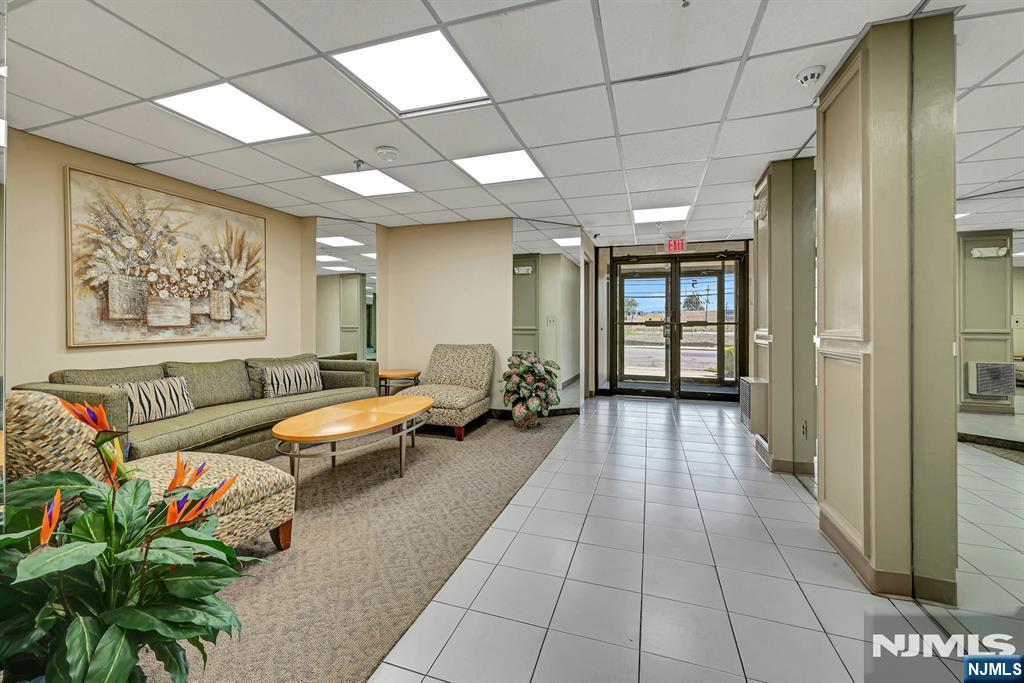 Apartment building lobby with a tiled walkway, furnished seating area, and glass entrance doors.