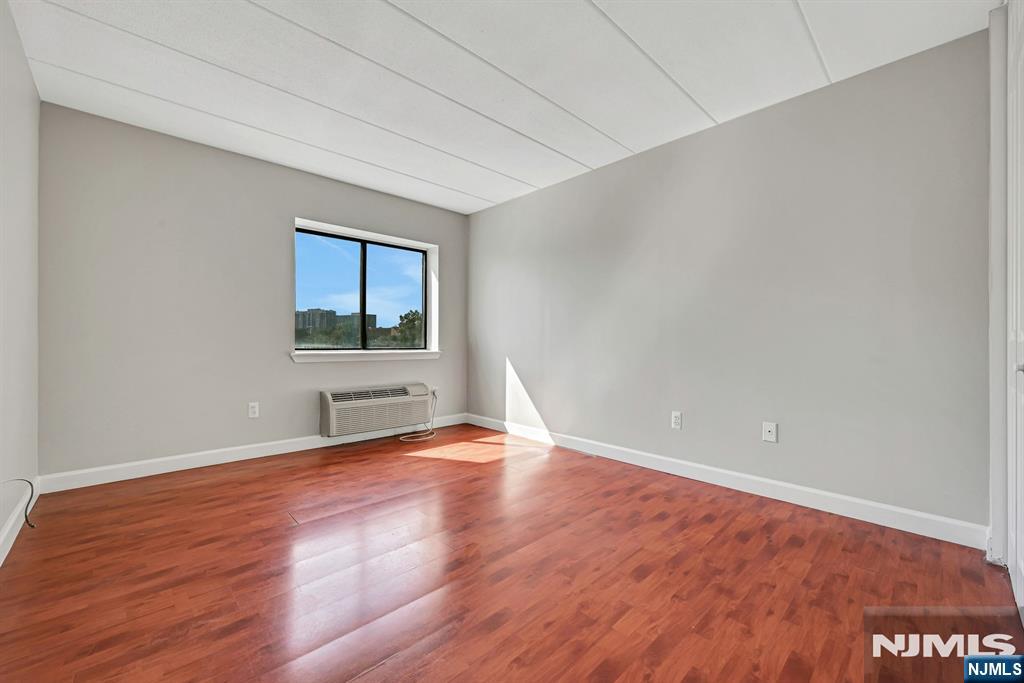 Empty room with reddish wood flooring, gray walls, and a window above a through-wall air conditioner.