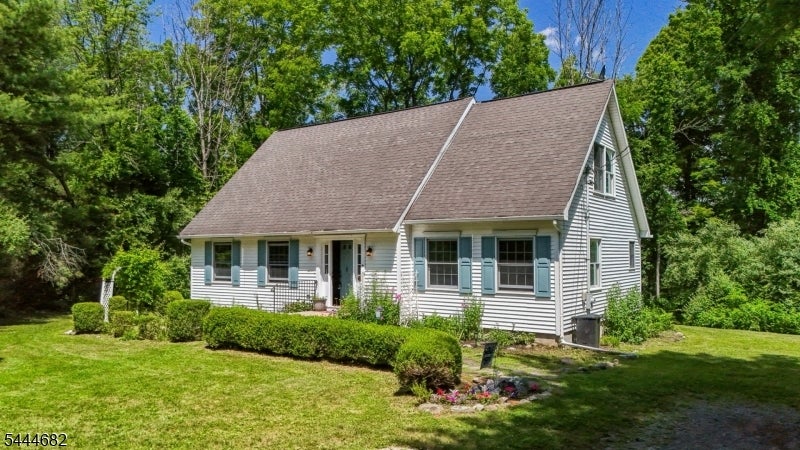 White house with blue shutters, a steep roof, and a landscaped lawn among mature trees.