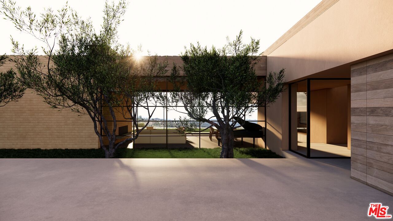 Modern home courtyard with mature trees, expansive glass windows, and a broad concrete patio.