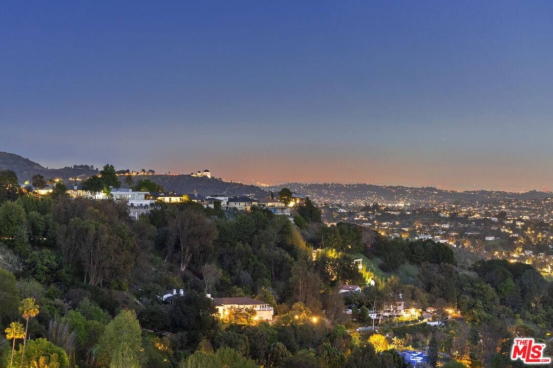 Panoramic view of hillside homes and illuminated Los Angeles beneath a blue dusk sky.