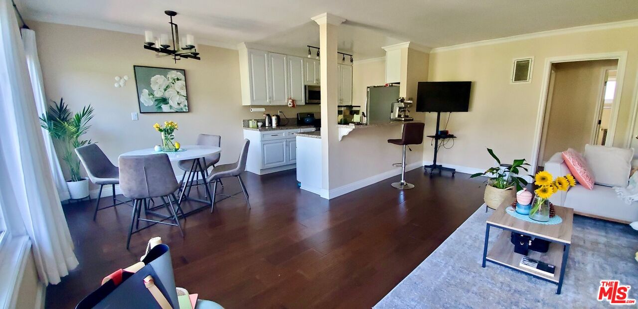 Open-plan living and dining area with dark wood floors, white kitchen cabinetry, and a round dining table.