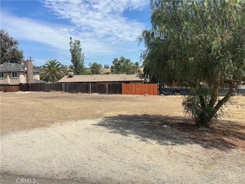 Cleared dirt lot with a fenced boundary and mature trees.