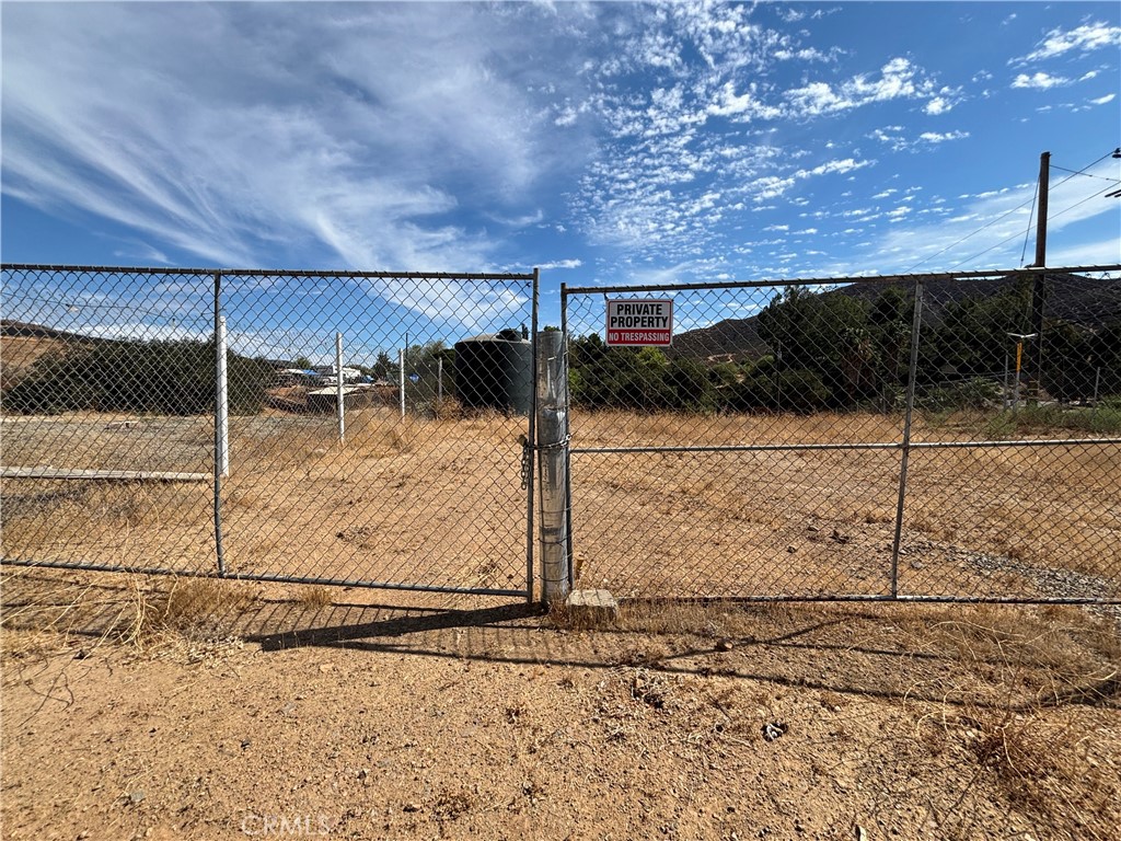Dry vacant lot behind a chain-link fence, with a private property sign and low hills beyond.