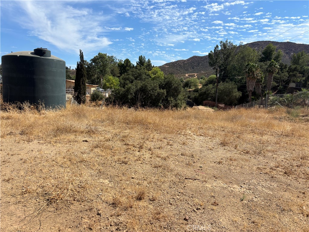 Vacant dry lot with golden grass, a large black water tank, trees, and hills in the background.