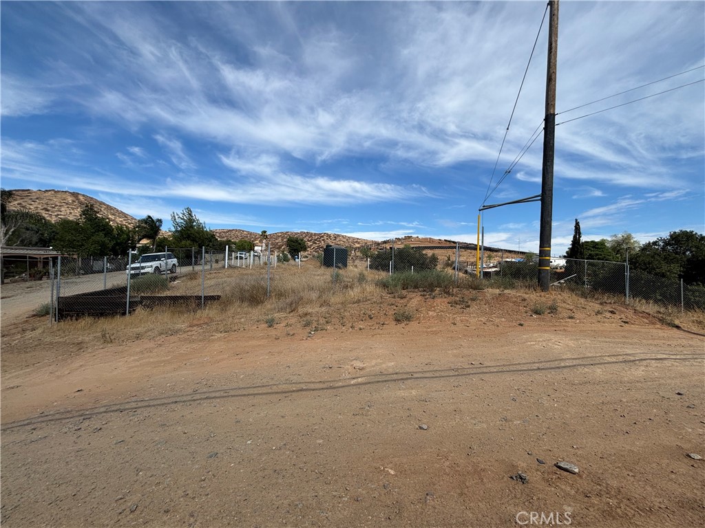 Vacant dirt lot with chain-link fencing, a utility pole, and low hills in the distance.