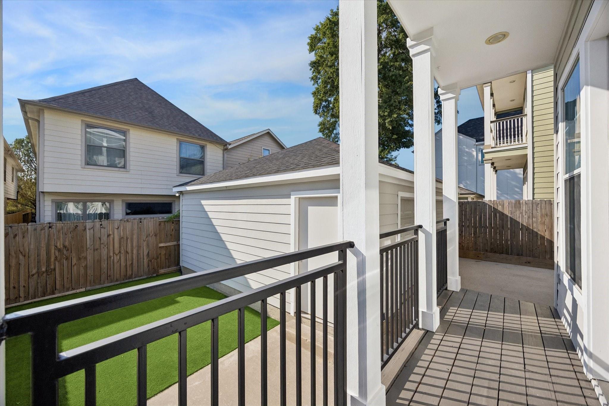 Covered deck with dark railings overlooks a fenced yard with artificial turf.
