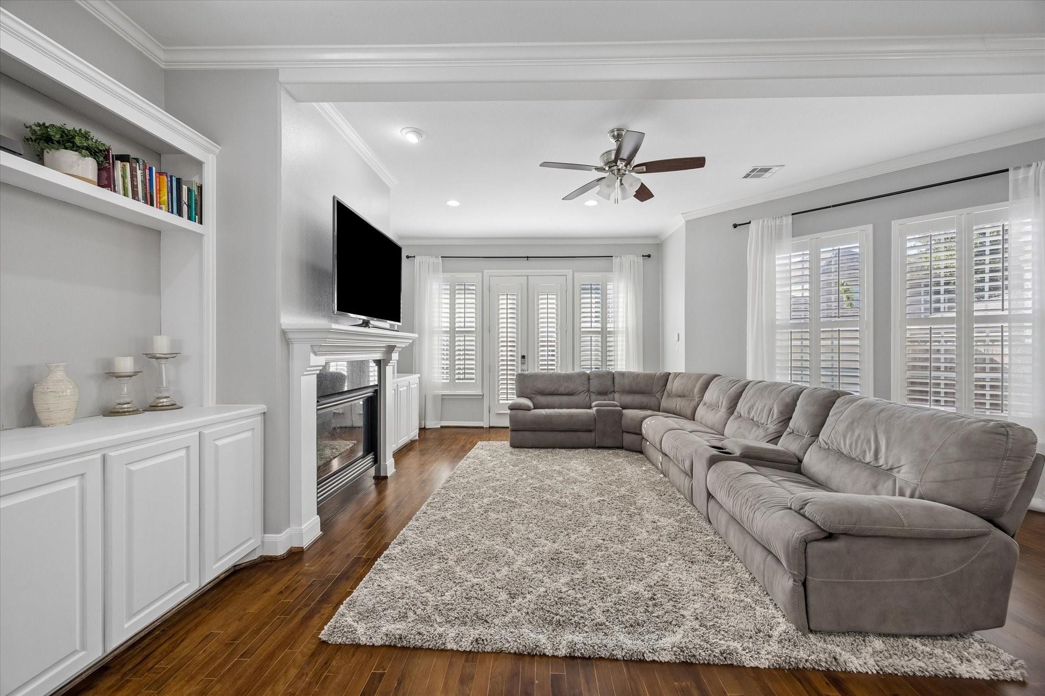 Living room with a large sectional, fireplace, built-in shelving, and plantation shutters.