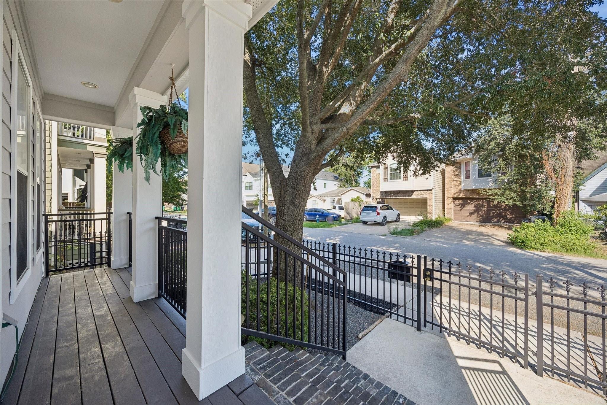 Front porch with white columns and black railings overlooking a leafy street.