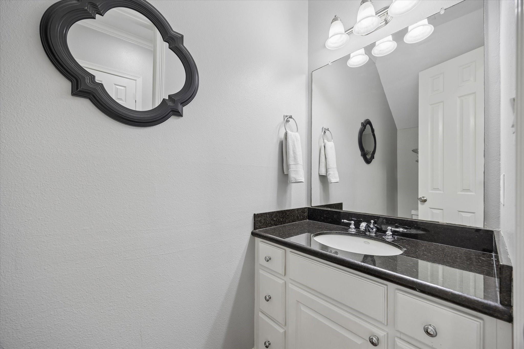Bathroom vanity with a dark countertop, white cabinetry, and an ornate black-framed mirror.